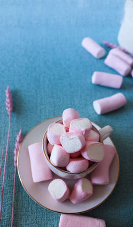 Sweet pink marshmallows on blue background. A marshmallow is shaped like a heart. Along with dried pink flowers. Female image, adorable and with an ideal shape for stories and square post.の写真素材