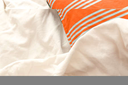 Orange and white striped towel on white bedding, top view. Space for textの写真素材