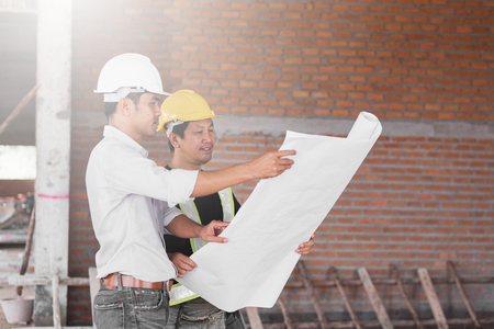 engineer working on checking progress of construction with blueprint at construction siteの写真素材