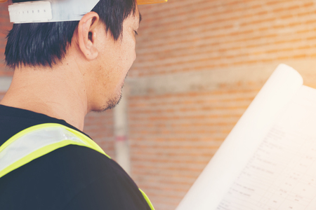 engineer working on checking progress of construction with blueprint at construction siteの写真素材
