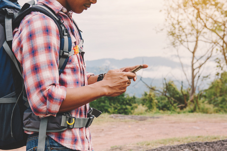 Hiking man with backpack using phone in mountains, Travel lifestyle success concept adventureの写真素材
