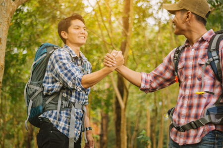 Hiking man helping each other hike up on traveling with backpack. Giving a helping hand, Travel lifestyle success concept adventureの写真素材
