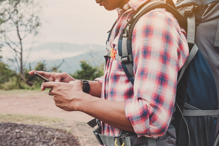 Hiking man with backpack using phone in mountains, Travel lifestyle success concept adventureの写真素材