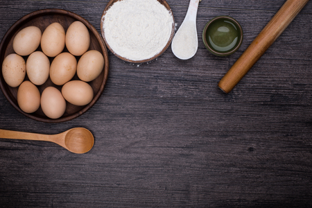 Wooden background with baking ingredients (eggs, flour and rolling pin) over rustic texture. Top view. Space for text. Food or cooking concept.の写真素材