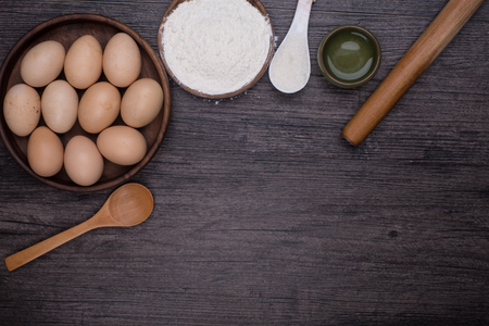 Wooden background with baking ingredients (eggs, flour and rolling pin) over rustic texture. Top view. Space for text. Food or cooking concept.の写真素材