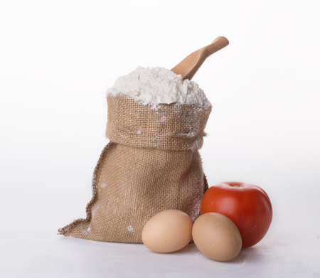 Flour in bowl with eggs and rolling pin over white backgroundの写真素材