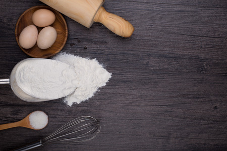 Wooden background with baking ingredients (eggs, flour and rolling pin) over rustic texture. Top view. Space for text. Food or cooking concept.の写真素材