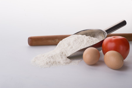 Flour in bowl with eggs and rolling pin over white backgroundの写真素材