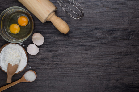 Wooden background with baking ingredients (eggs, flour and rolling pin) over rustic texture. Top view. Space for text. Food or cooking concept.の写真素材