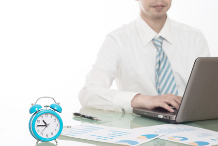 young crazy businessman punching switching off alarm clock sitting at office desk working with computer laptop in deadline project concept and business stress conceptの写真素材