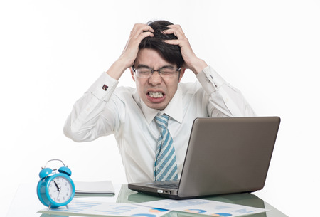 young crazy businessman punching switching off alarm clock sitting at office desk working with computer laptop in deadline project concept and business stress conceptの写真素材