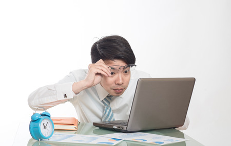 young crazy businessman punching switching off alarm clock sitting at office desk working with computer laptop in deadline project concept and business stress conceptの写真素材