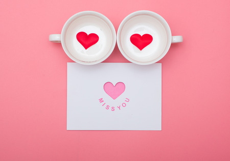 Cup and valentines day card on pink background