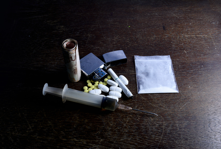 the drug in syringe  put on the table  with the money , cigarette,lighter and yellow - white medicine,white powder drug in bagの写真素材