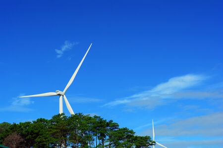 The white electric wind turbine with blue sky and trees  at Petchaboon,Thailandの写真素材