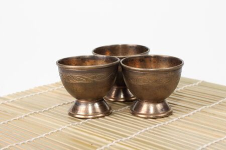 Three aged steel cups on bamboo mate