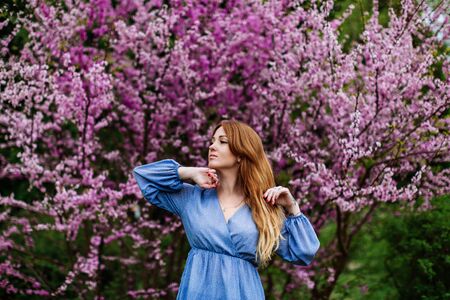 Beautiful dreaming redhead woman in spring time blossom cherrytrees garden.の写真素材