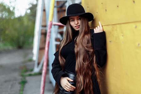 Young beautiful fashionable woman in black hat, with long hair posing on blurry background. Female...
