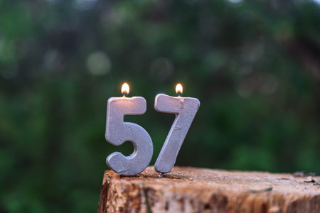 Silver festive candles forming the number 57. Burning metallic digits standing on a wooden texture...