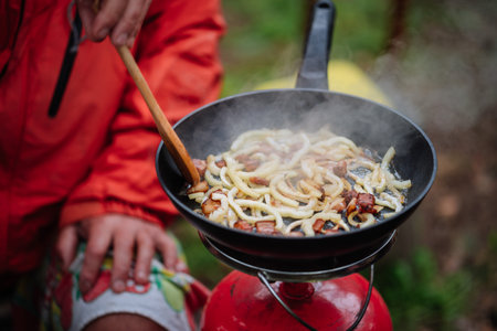 Close-up of sliced onion and pork fat being fried in a pan on a portable camping stove. Traditional...