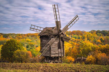 Traditional old wooden windmill standing on a rural hillside surrounded by colorful autumn forest....