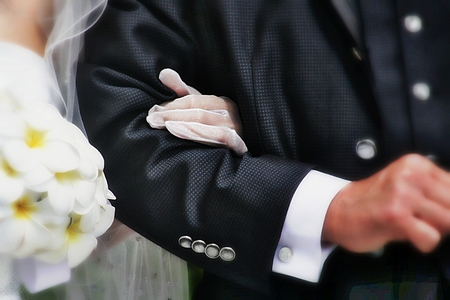 A bride with a bouquet of flowers in one hand, and her other hand  on the arm of her groomの写真素材