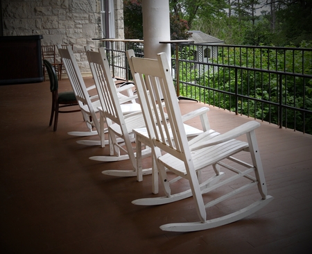 Three white rocking chairs lined up in a balcony of a building facing the gardenの写真素材