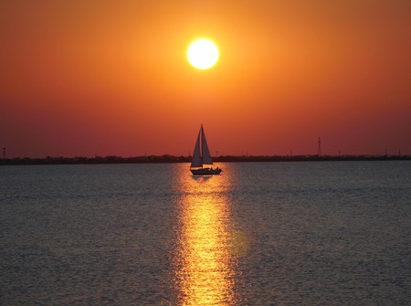 A sailboat passes through the golden reflections cast by a full round sunsetの写真素材