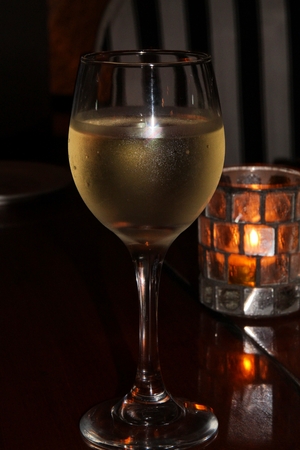 White wine in a wine glass on the table, with a candlelit backgroundの写真素材
