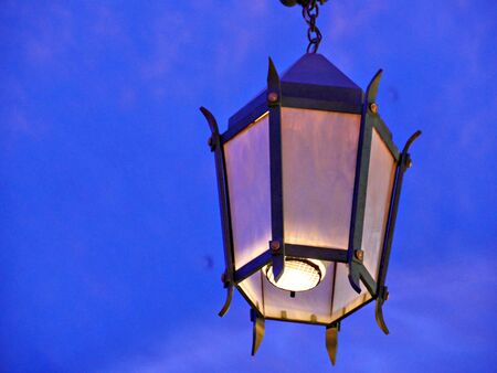 Close upward shot of a lighted lamp post, with blue backgroundの写真素材