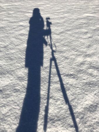 Shadow of a girl with a camera and tripod in the snow