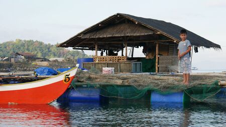 Banay Banay, Davao Oriental, Philippines - March 2016: A boy stands on a bamboo platform at fish pens in a Philippine fishing village.のeditorial素材