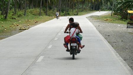 Governor Generoso, Davao Oriental, Philippines-March 2016: A man drives a motorcycle with two children behind him at a national highway in the Philippines.のeditorial素材