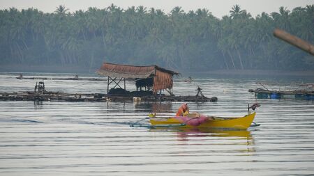 Banay Banay, Davao Oriental, Philippines - March 2016: A yellow outrigger boat glides away from the fish pens at Punta Linao fishing village in the southern Philippines.のeditorial素材