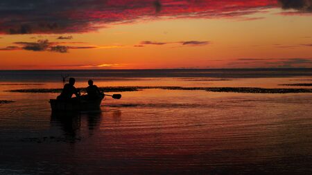Silhouette of two boaters in the sea with dramatic sunset background