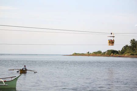 Surigao del Sur, Philippines- August 2014: Wide river shot with a cable car in the air and boater rowing in the water in Carrascal, Surigao del Sur.のeditorial素材