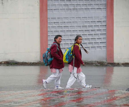 Manali, Himachal Pradesh, India- March 2018: Two students walk in the rain in a street in Manali.のeditorial素材