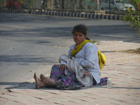 New Delhi, India- March 2018: A woman with a small baby sits on a streetside in New Delhi.のeditorial素材