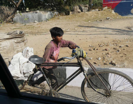 New Delhi, India- March 2018: A boy pushes a bicycle loaded with sacks at a roadside in New Delhi.のeditorial素材