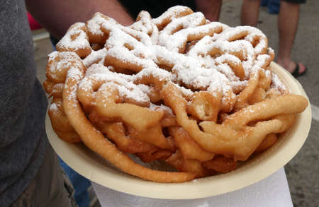 A hand holding a plate of funnel cake with powdered sugar on topの写真素材