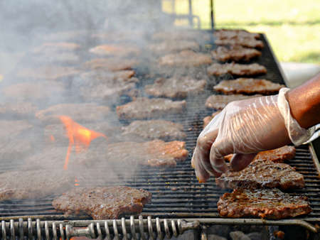 A hand flipping burgers with a spatula over a flaming grillの写真素材