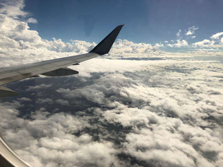 An airplane wing sticks out surrounded by white fluffy clouds in the skies