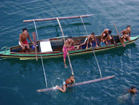 CAGAYAN DE ORO CITY, PHILIPPINESâCIRCA JULY 2009:  A man and some boys in a boat and in the water get ready to dive for coins from passengers in a ship at the Cagayan de Oro city pier.のeditorial素材