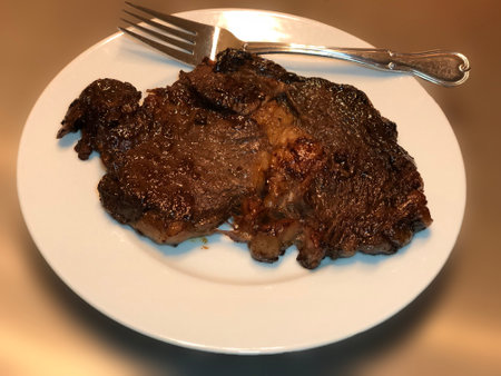 Grilled steak on a white plate with a fork and knife.の写真素材