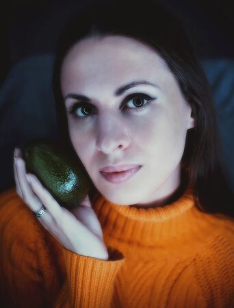 Young caucasian woman holding fresh avocado fruit near face