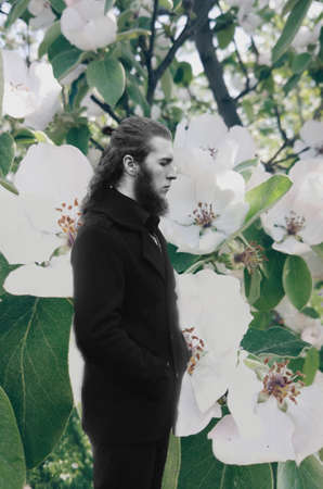 Male portrait outdoor surrounded by blooming flowers.