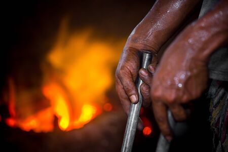 Unsafe worker hands. A local steel machine parts making yard worker melting scrap on hot furnace.の写真素材