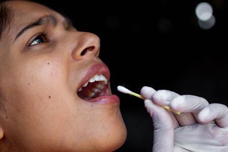 Doctor's hand taking Saliva test from young woman's mouth with Cotton Swab. Coronavirus Throat...