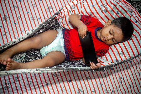 Before going to sleep a child is lying a homemade hammock and watching cartoons using a smartphone tab. Kids playing with smartphone. Mobile phone and internet addiction concept.の写真素材