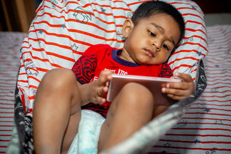Before going to sleep a child is lying a homemade hammock and watching cartoons using a smartphone....